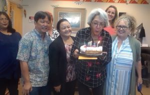 Photo of Pomai blowing out candles on a cake with other staff members looking on