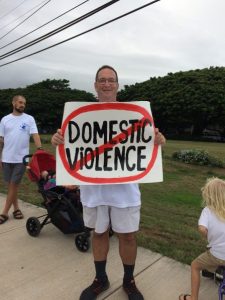 Photo of Brian holding sign that says, "No Domestic Violence"